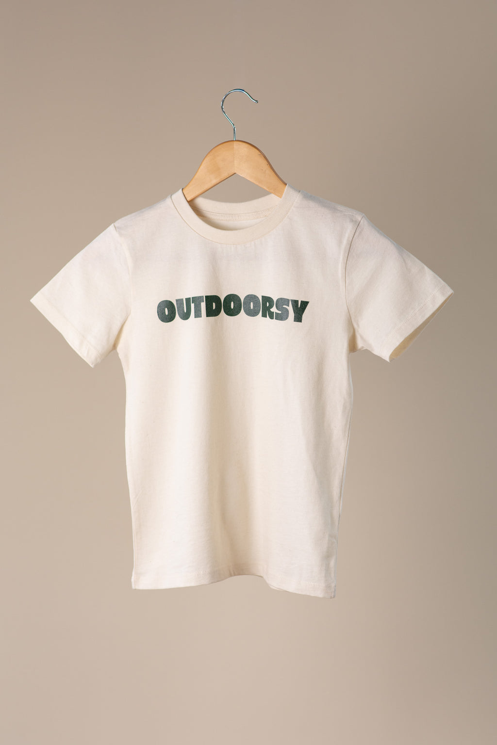 White t-shirt with 'OUTDOORSY' text on a hanger against a beige background
