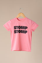 Pink t-shirt with 'STOMP STOMP' text on a wooden hanger against a beige background