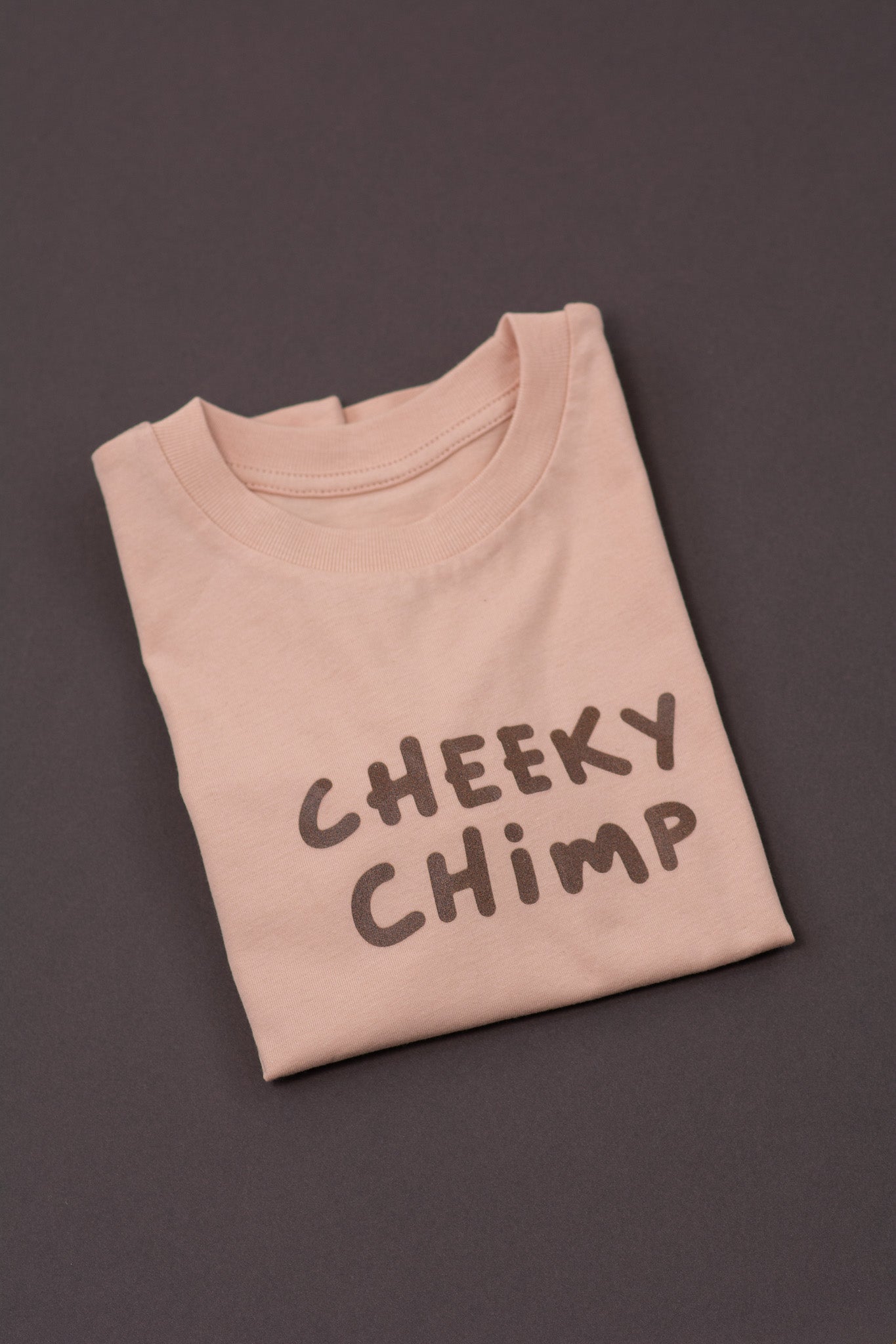 Folded peach t-shirt with 'CHEEKY CHIMP' text on a dark background