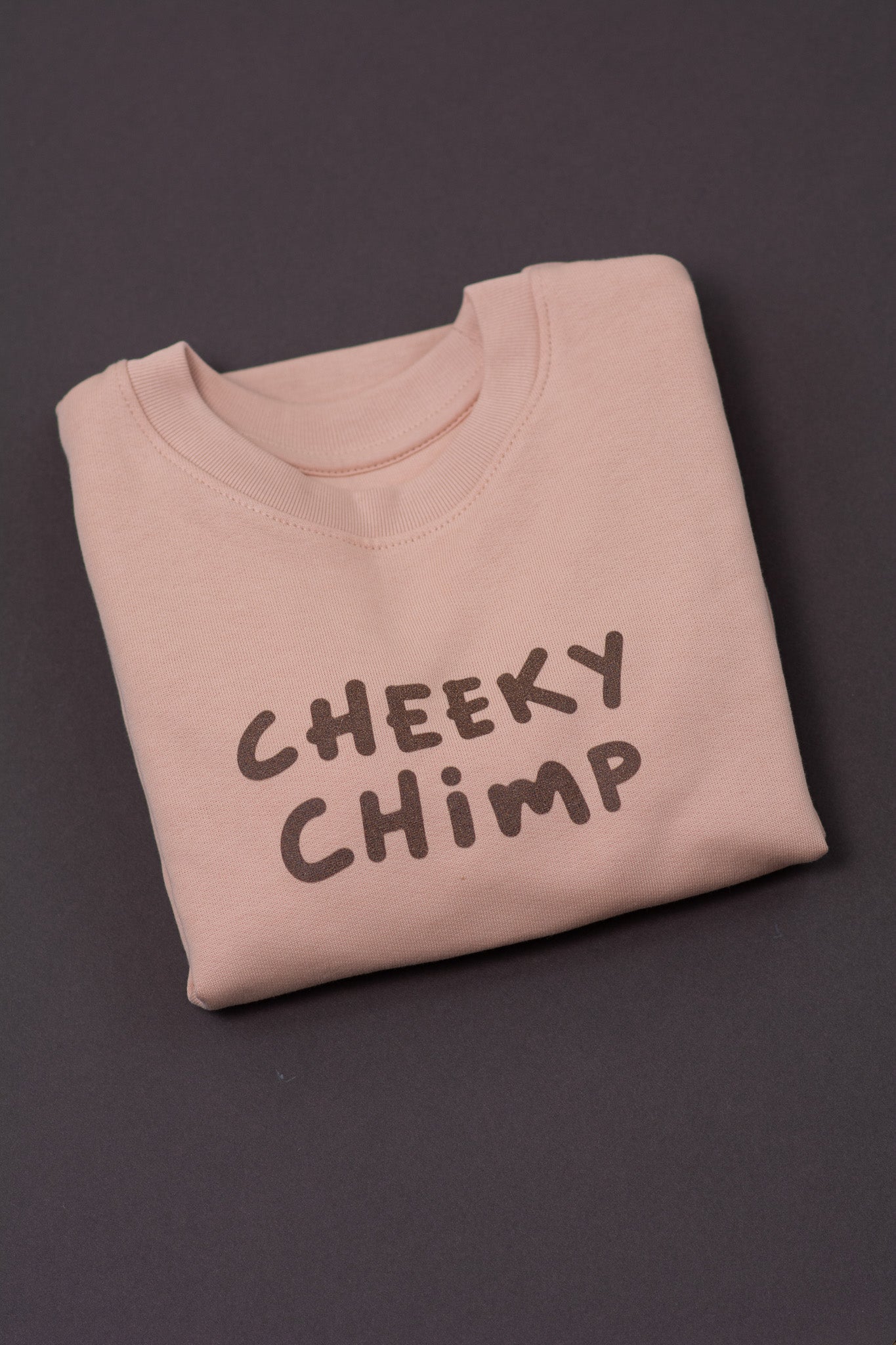 Folded peach sweatshirt with 'CHEEKY CHIMP' text on a dark background