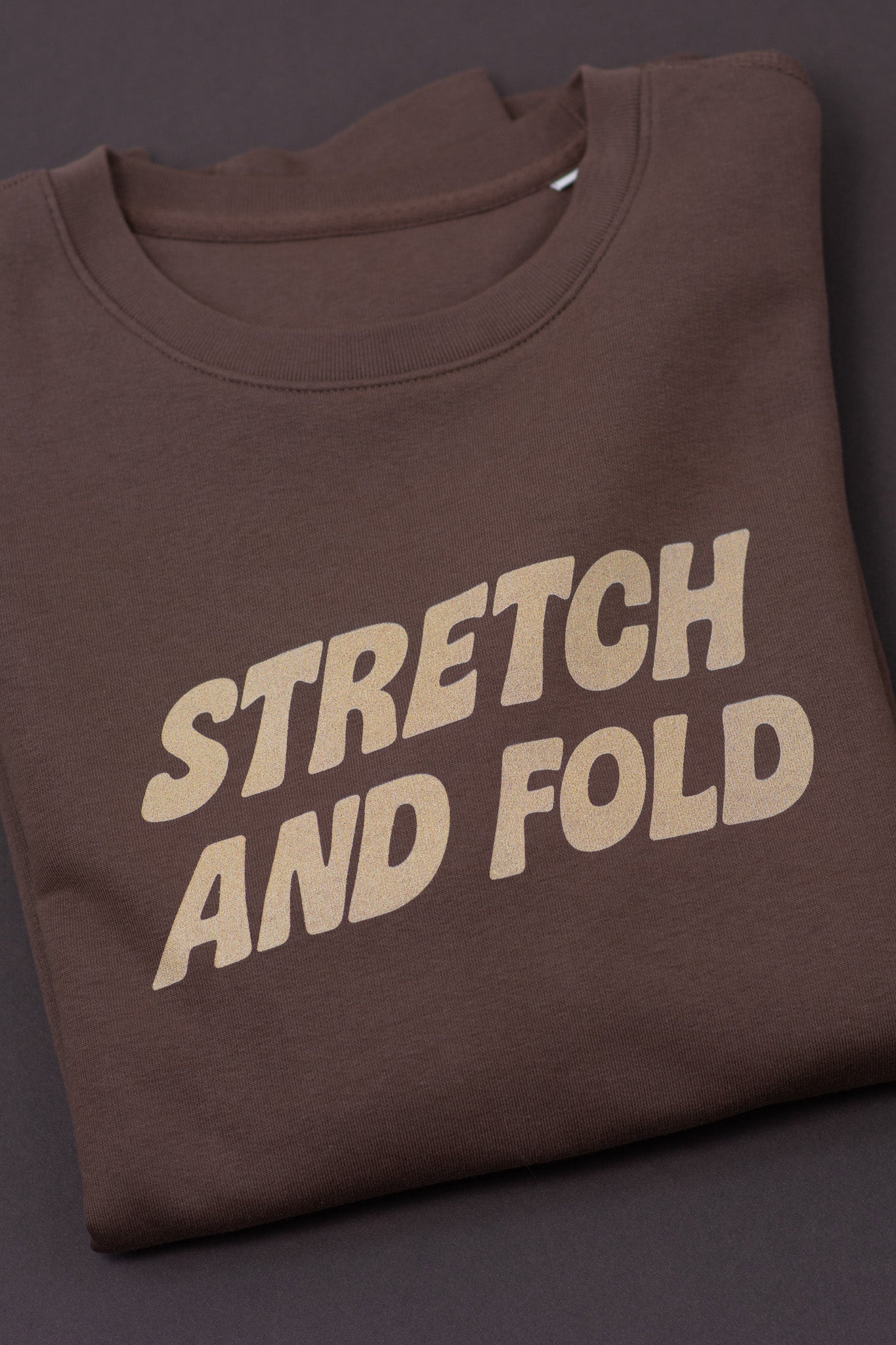 Brown t-shirt with 'STRETCH AND FOLD' text on a dark background