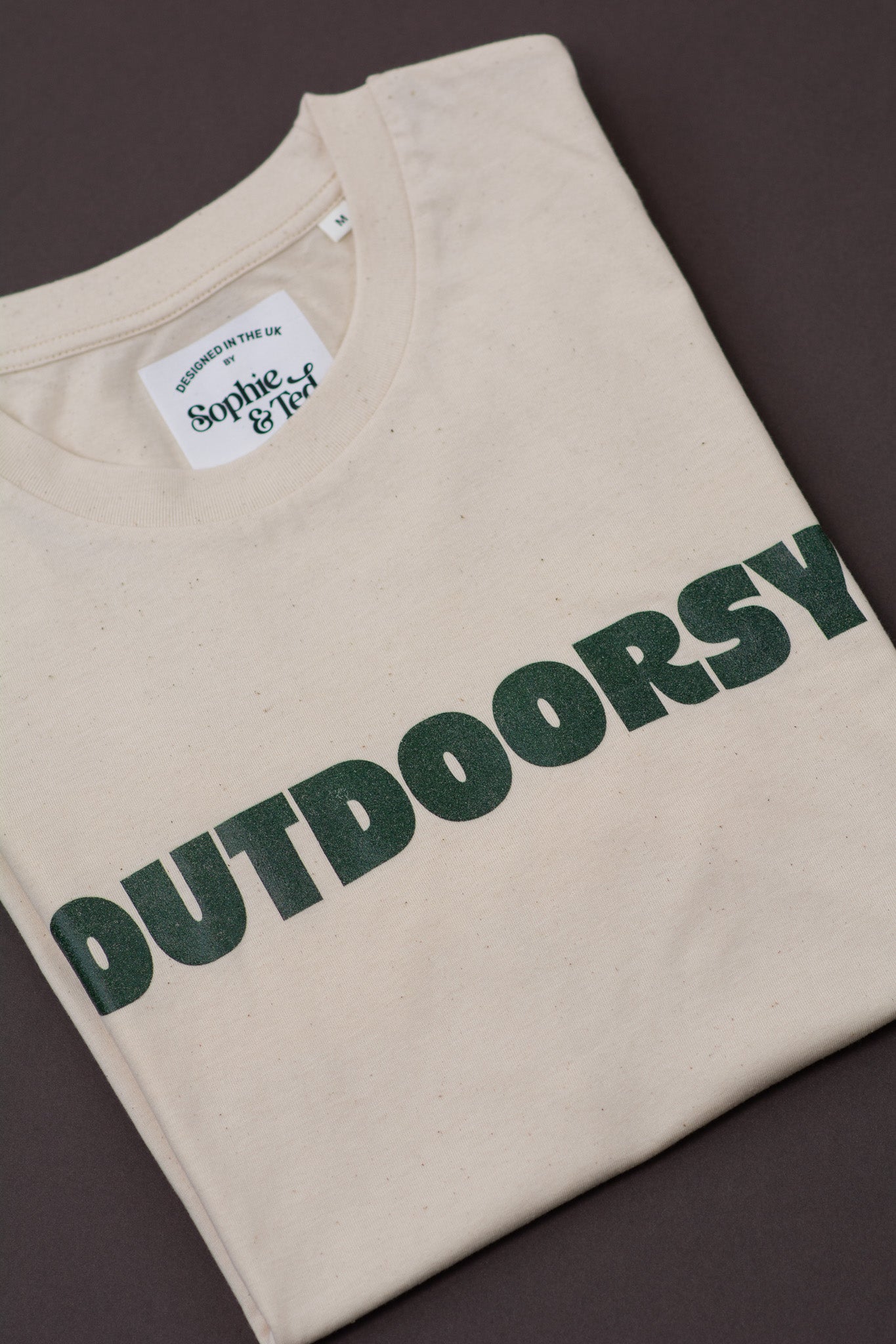 Beige t-shirt with 'OUTDOORSY' text in green on a dark background