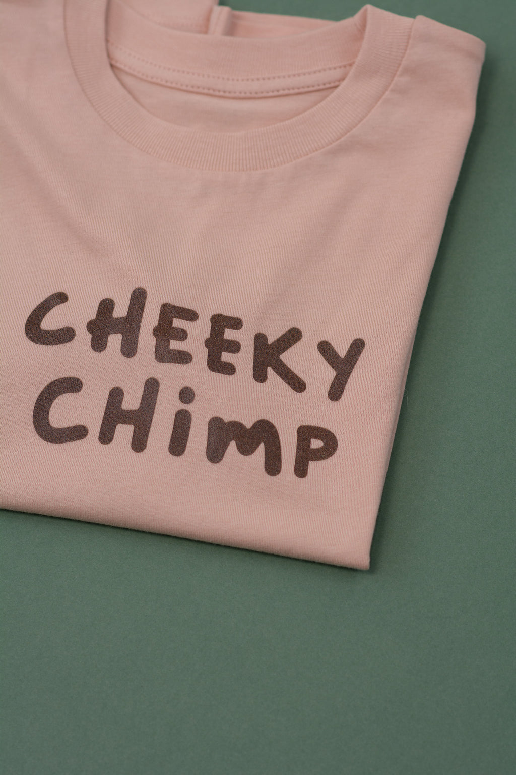 Folded peach t-shirt with 'CHEEKY CHIMP' text on a green background