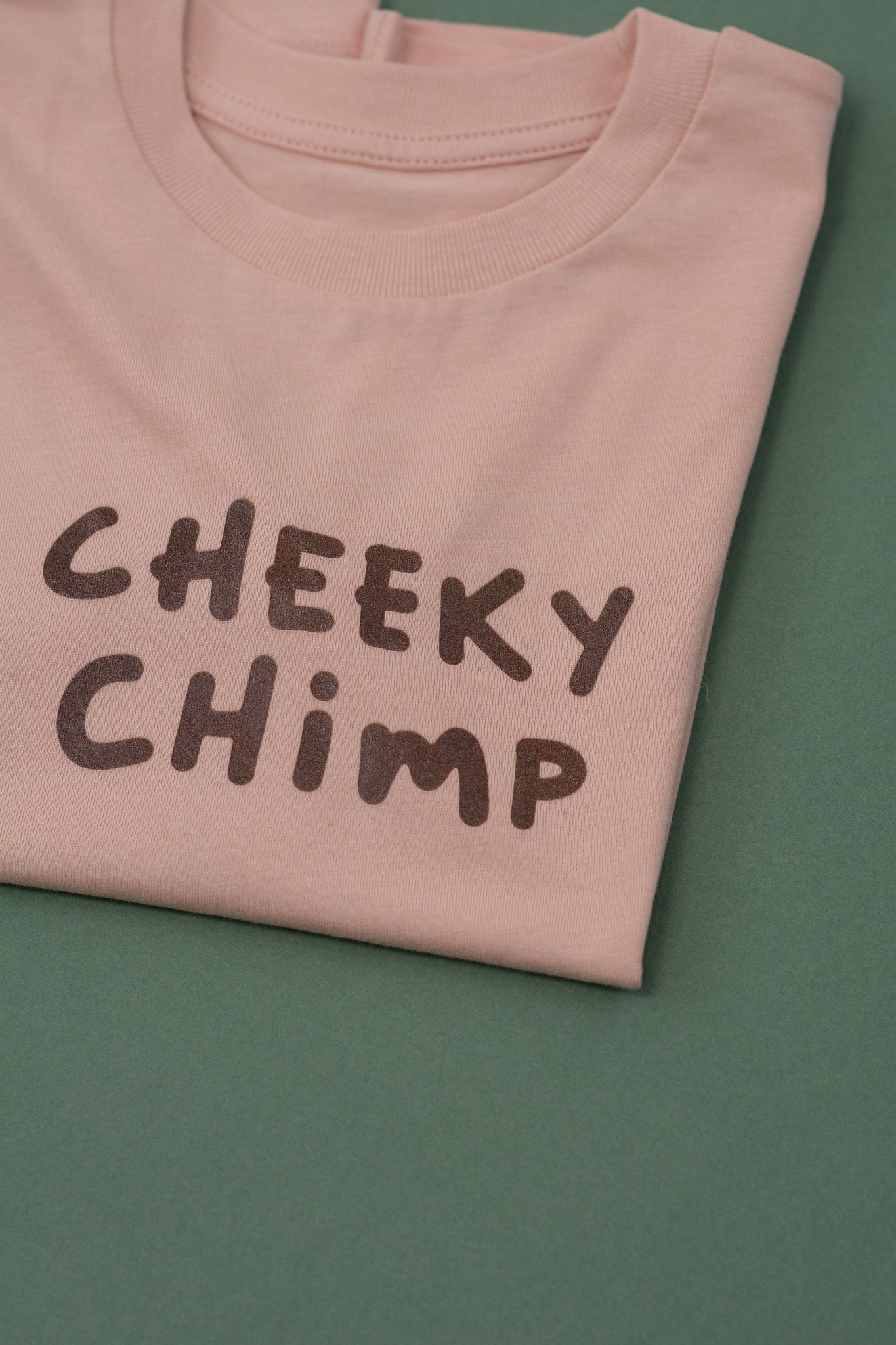 Folded peach t-shirt with 'CHEEKY CHIMP' text on a green background