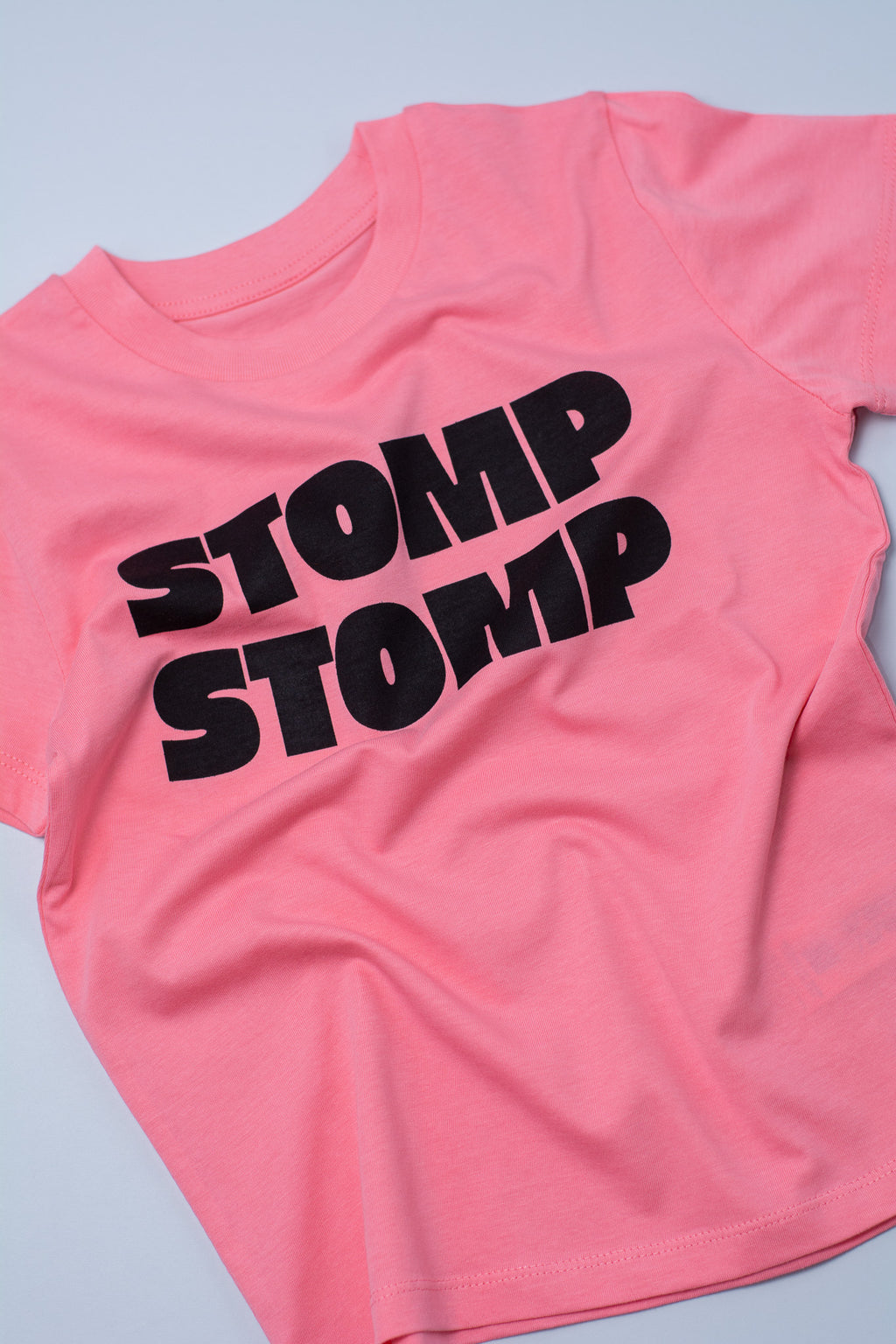Pink t-shirt with 'STOMP STOMP' text on a light grey background