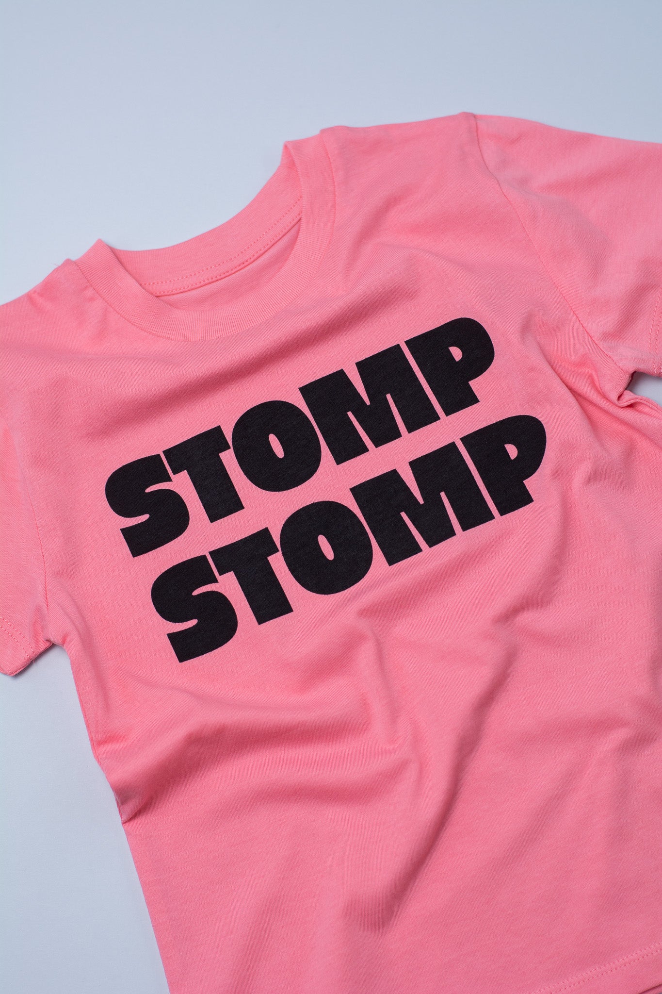 Pink t-shirt with 'STOMP STOMP' text on a light grey background