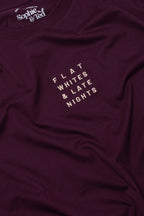 Maroon t-shirt with text 'FLAT WHITES & LATE NIGHTS' on a close-up of fabric texture
