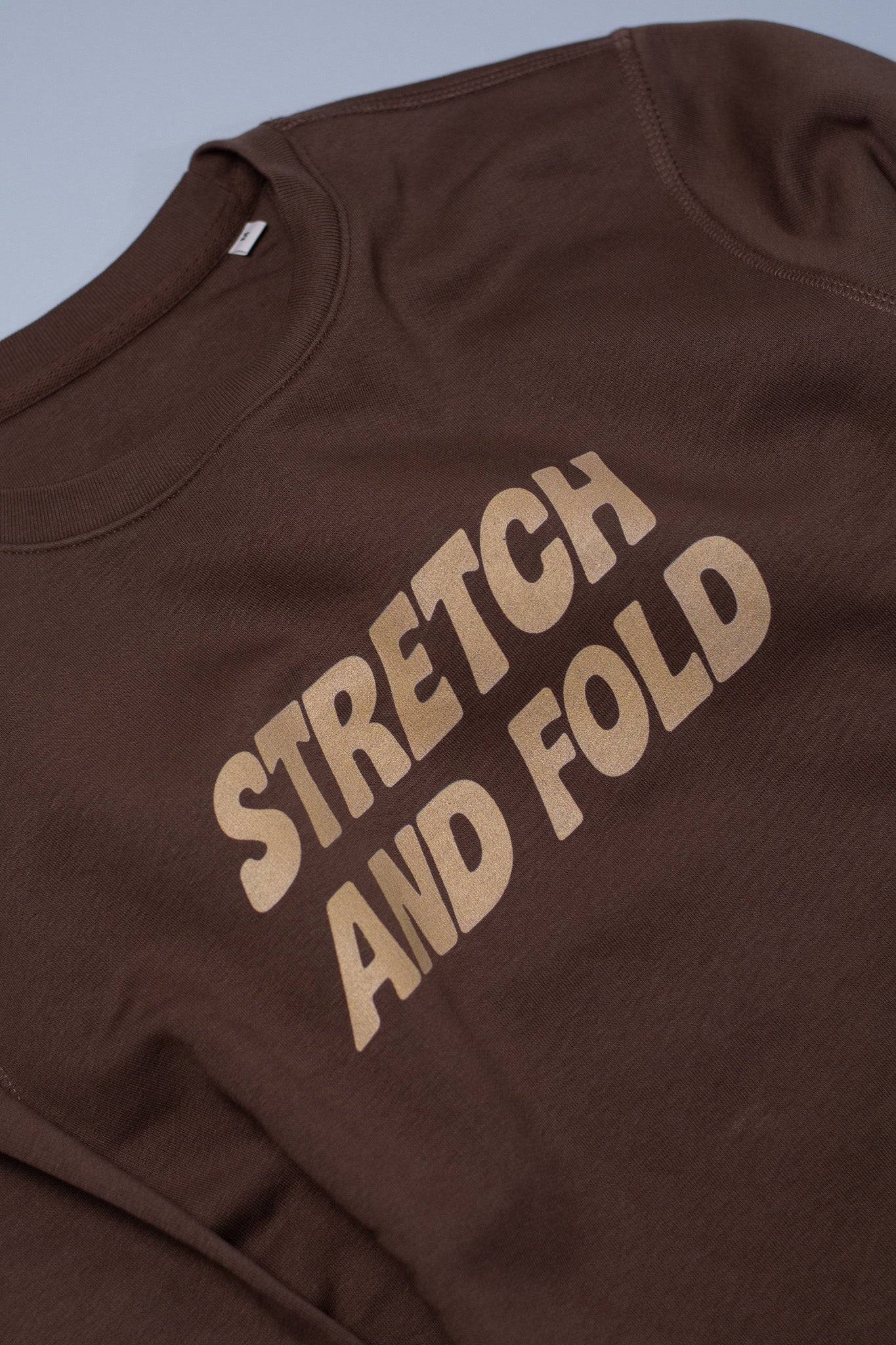 Brown sweatshirt with 'STRETCH AND FOLD' text on a plain background