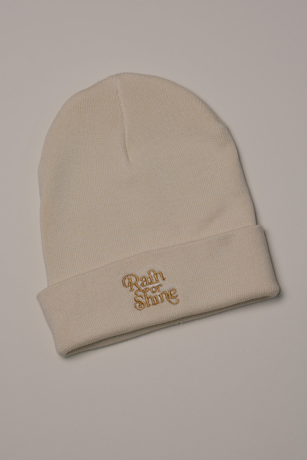 Beige beanie with 'Rain or Shine' embroidery on a light background