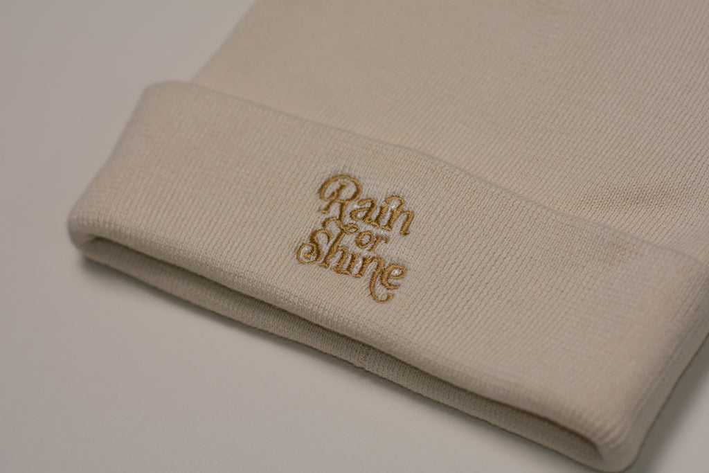 Beige beanie with 'Rain or Shine' embroidery on a light background