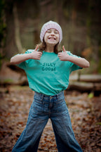 Person wearing a teal shirt with 'SILLY GOOSE' text, giving thumbs up outdoors.