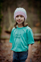 Child wearing a teal shirt with 'Silly Goose' text and a striped hat outdoors.