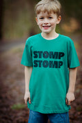 Child wearing a green t-shirt with 'STOMP STOMP' text outdoors.