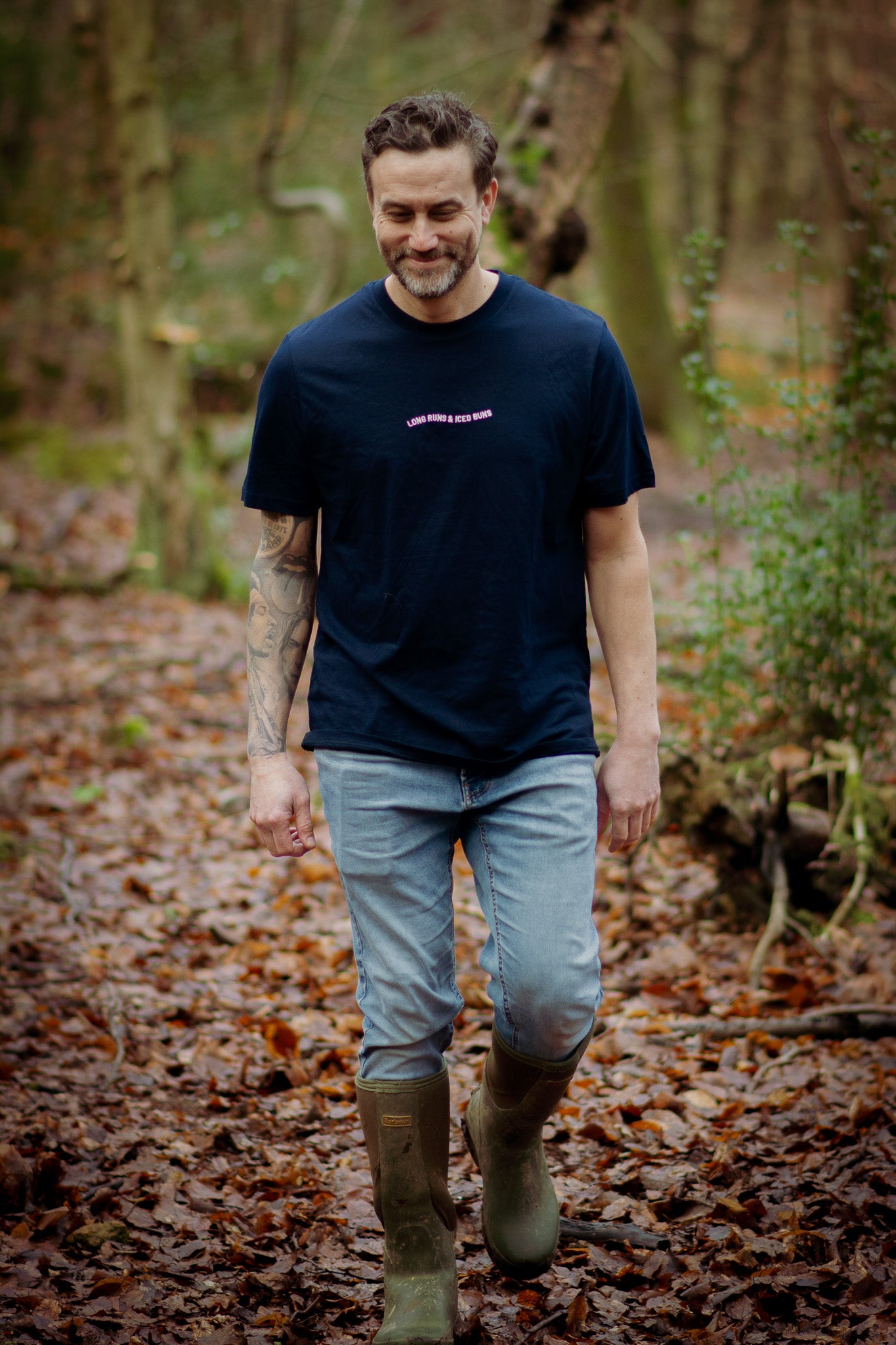 Man walking in a forest wearing a navy t-shirt and green boots.
