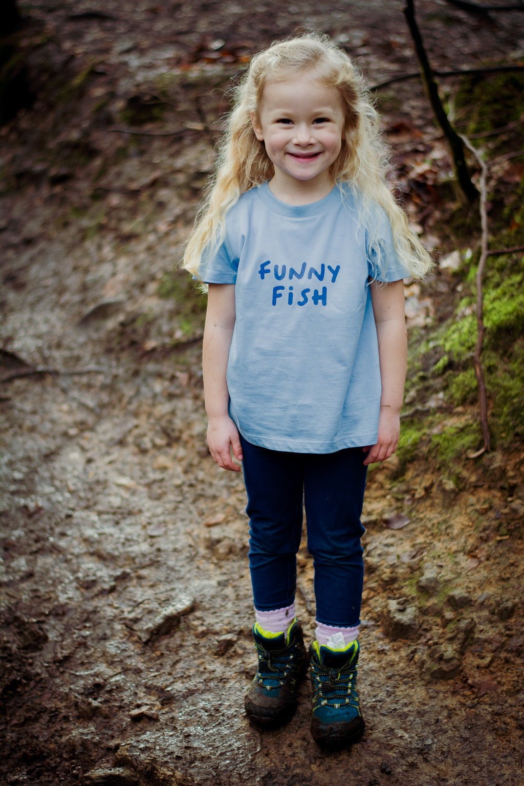 Child wearing a 'Funny Fish' t-shirt standing on a rocky surface.