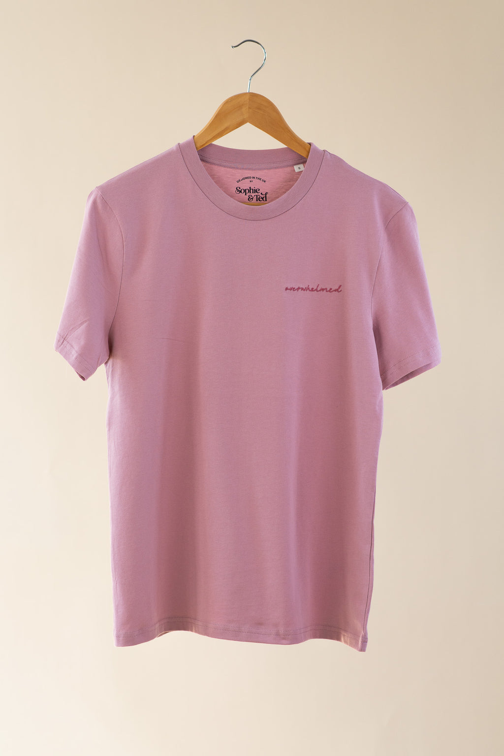 Pink t-shirt with text on a hanger against a beige background