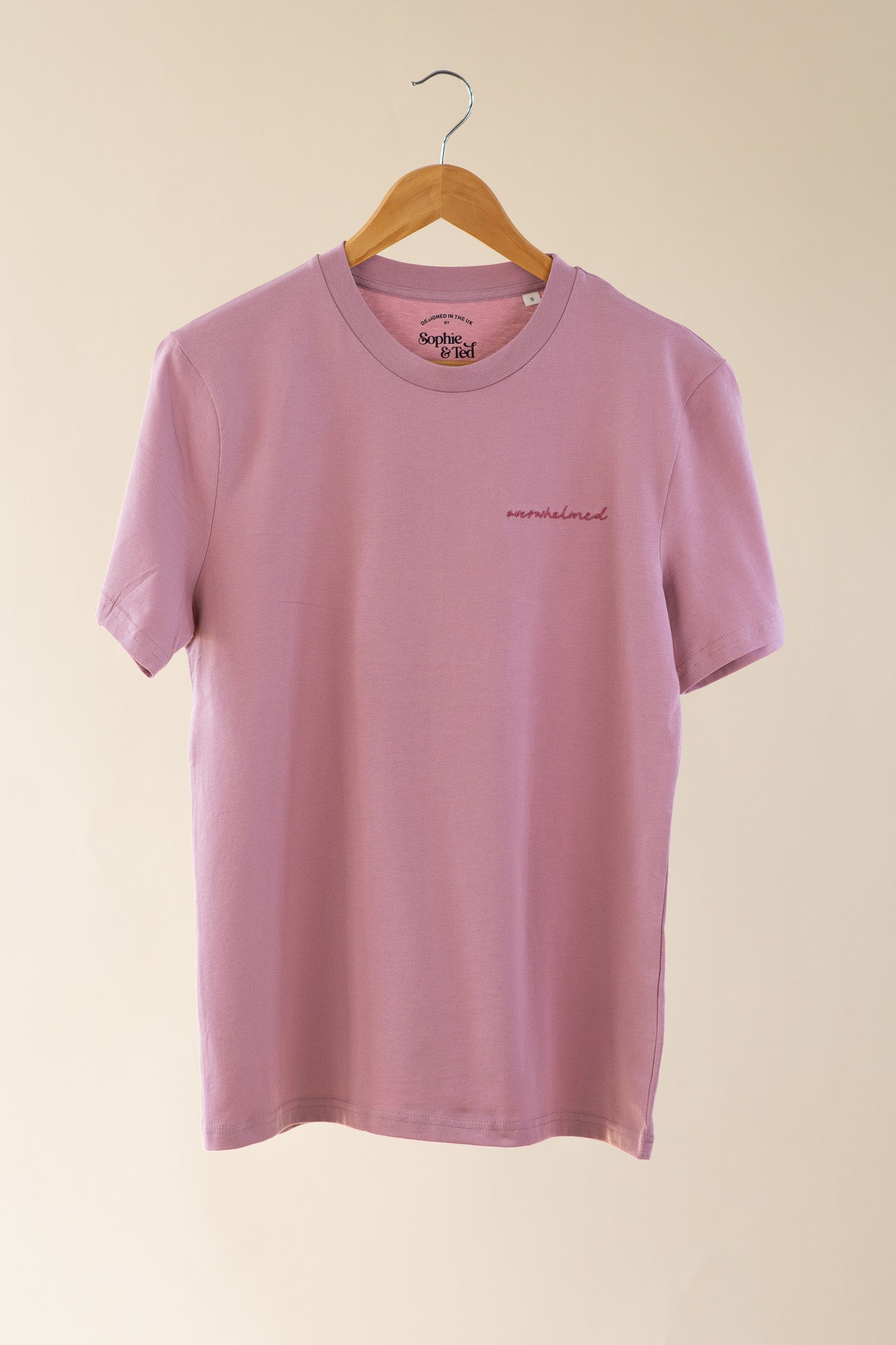 Pink t-shirt with text on a hanger against a beige background