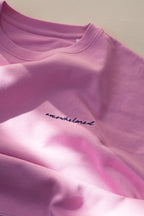 Close-up of a pink sweatshirt with 'overwhelmed' text on a light background