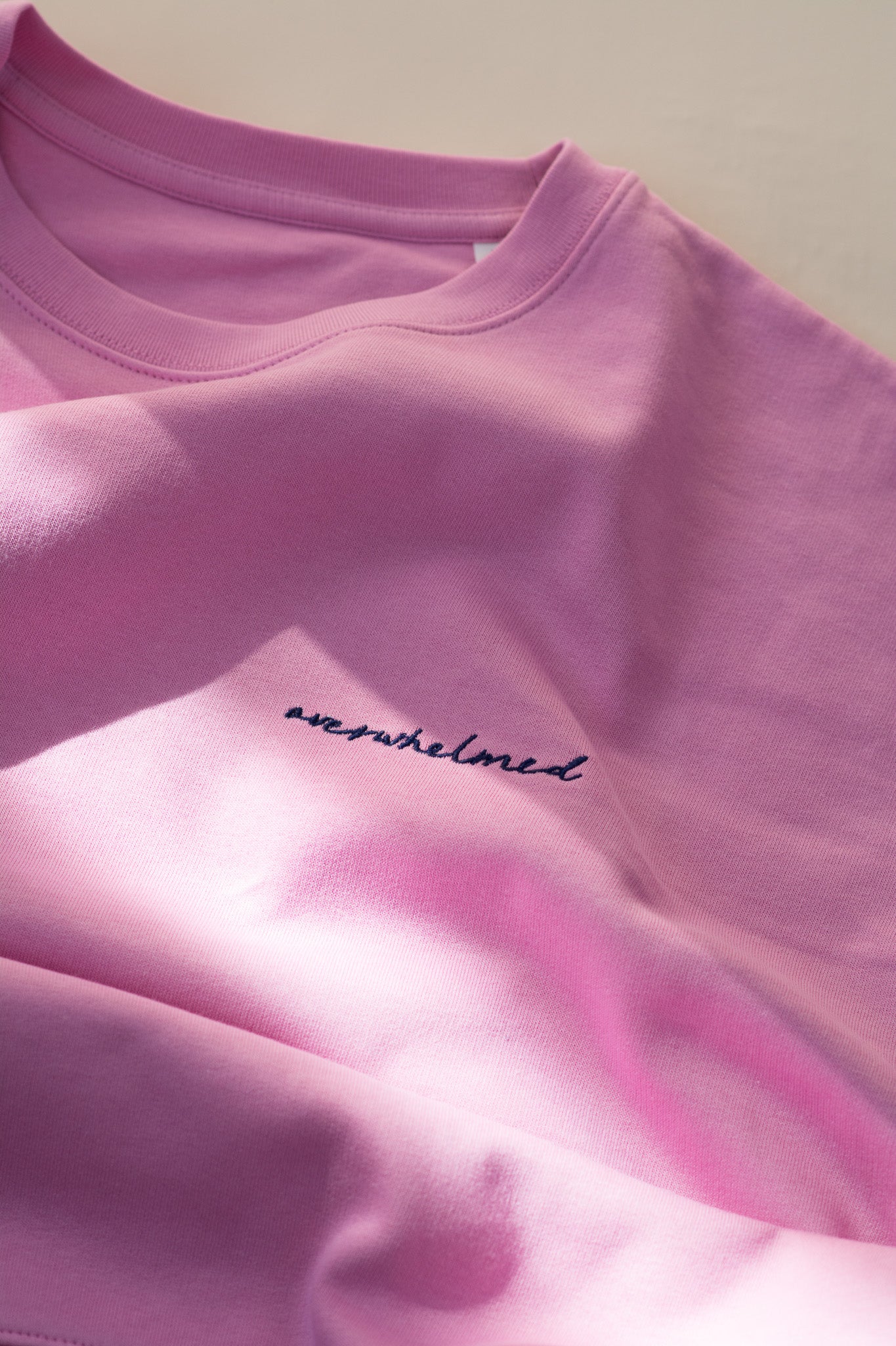 Close-up of a pink sweatshirt with 'overwhelmed' text on a light background