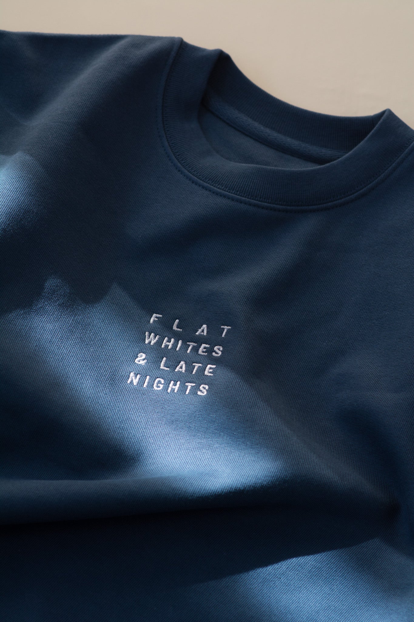 Navy blue sweatshirt with 'FLAT WHITES & LATE NIGHTS' text on a beige background