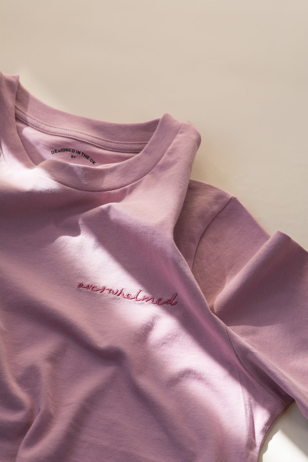 Pink t-shirt with 'overwhelmed' text on a light background