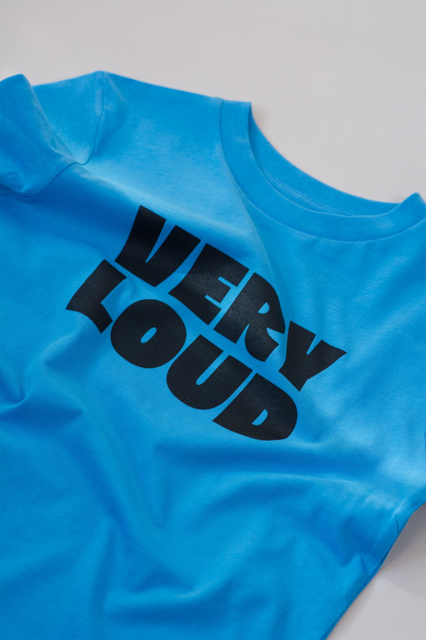 Blue t-shirt with 'VERY LOUD' text in black on a light gray background