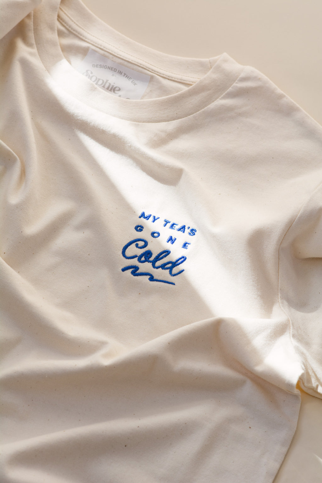 White t-shirt with blue text 'My tea's gone cold' on a light background