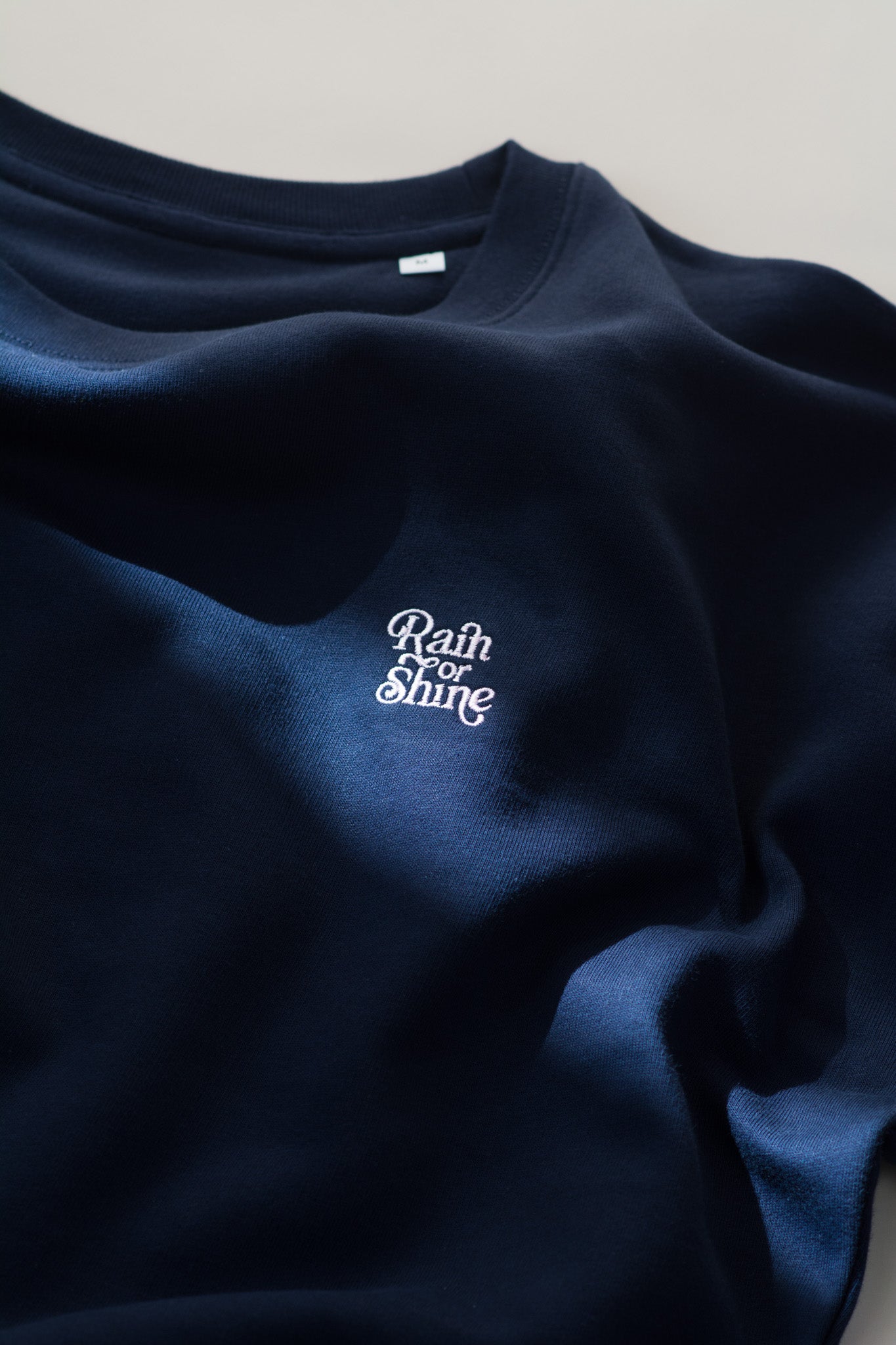 Navy blue sweatshirt with 'Rain or Shine' text on a light gray background