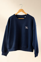 Navy blue sweatshirt with a logo on a wooden hanger against a beige background
