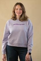 Woman wearing a light purple sweatshirt with text on a beige background