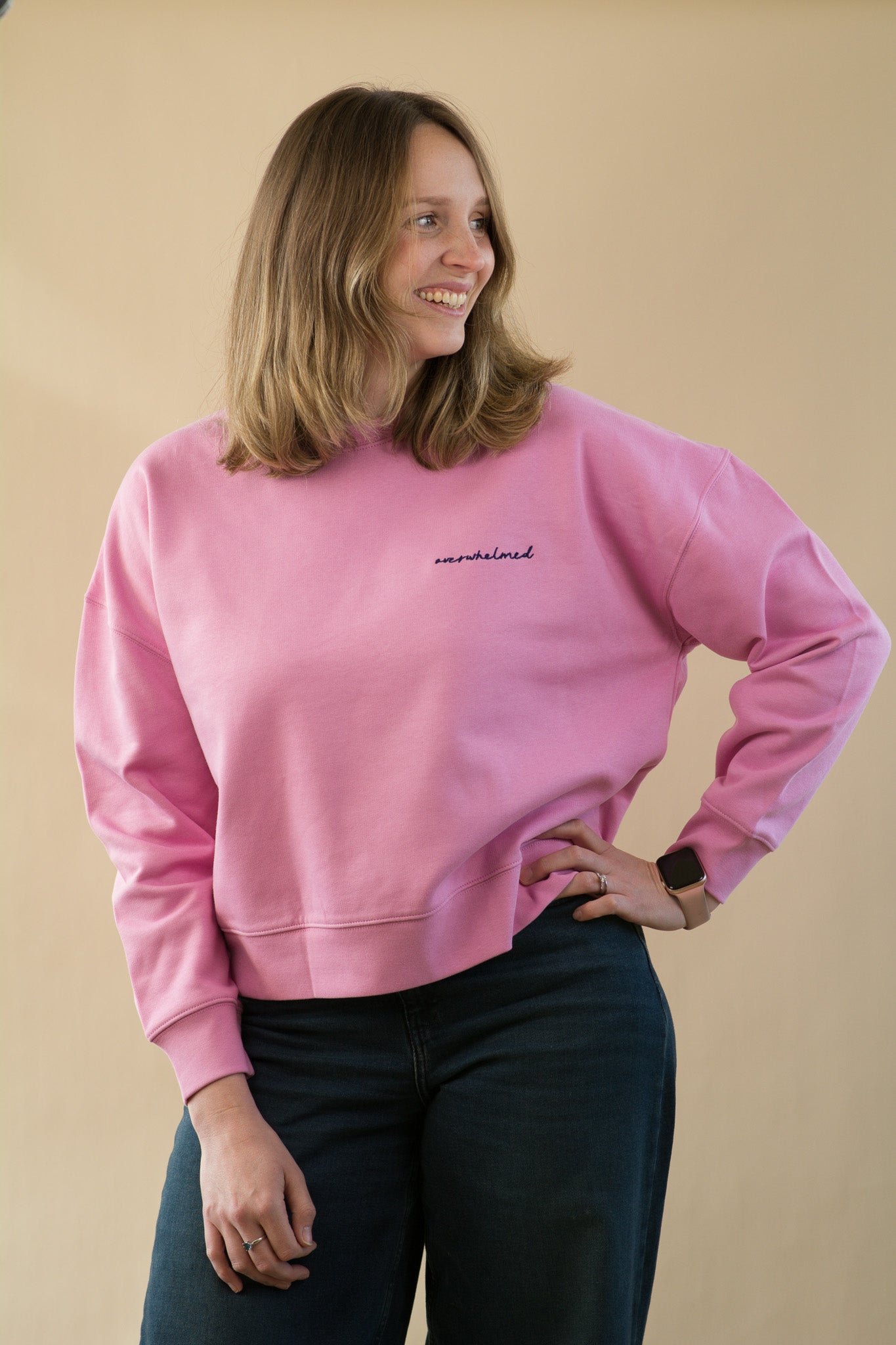 Woman wearing a pink sweatshirt with text on it against a beige background
