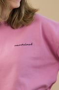 Person wearing a pink sweatshirt with text on it against a beige background