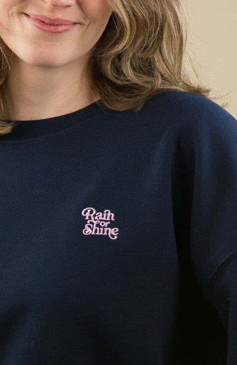 Woman wearing a navy blue sweatshirt with a logo on a beige background