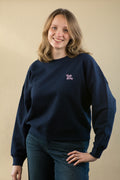 Woman wearing a navy blue sweatshirt with a small logo on a beige background