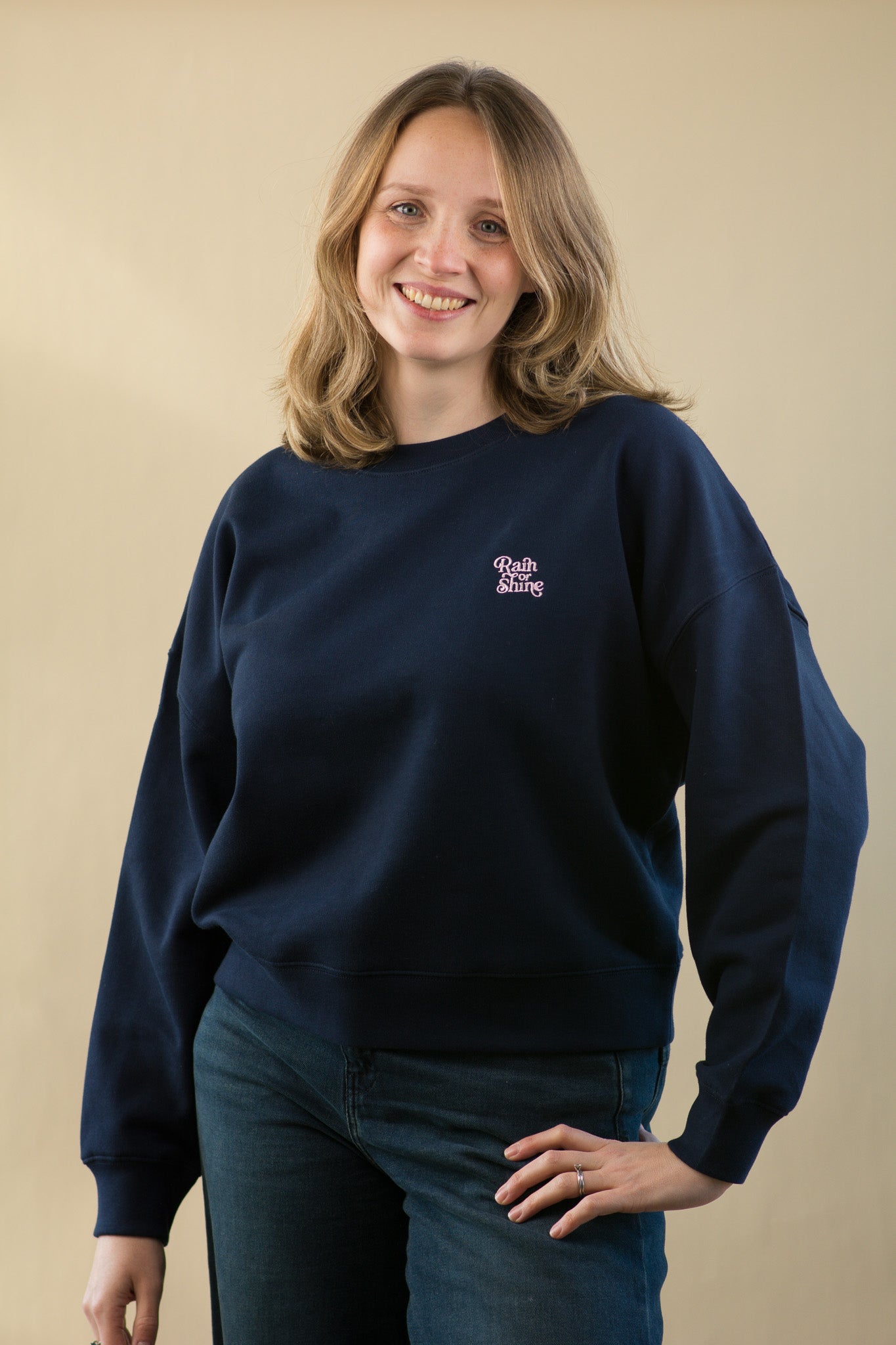 Woman wearing a navy blue sweatshirt with a small logo on a beige background