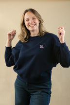 Person wearing a navy blue sweatshirt with a logo on a beige background