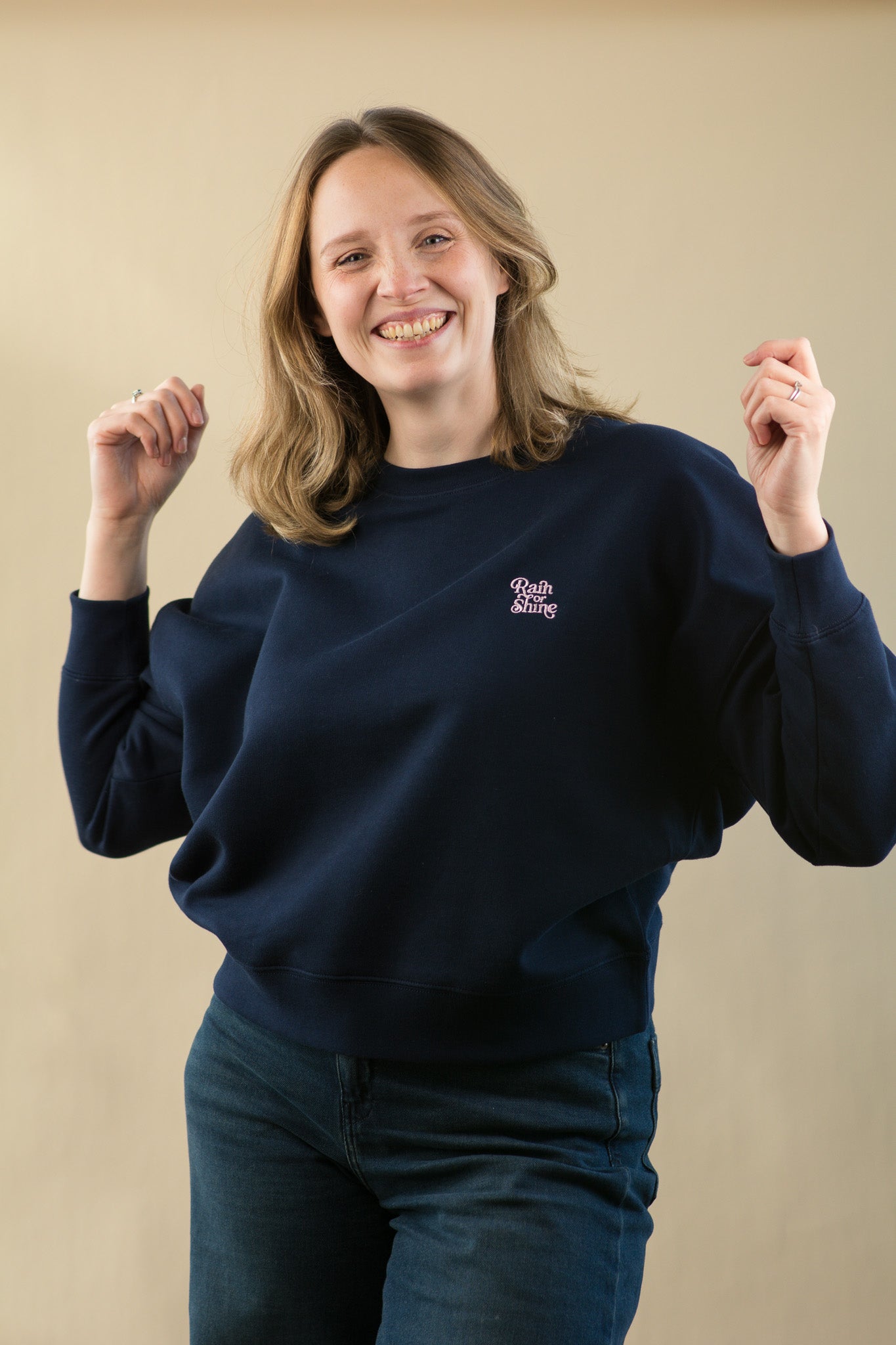 Person wearing a navy blue sweatshirt with a logo on a beige background