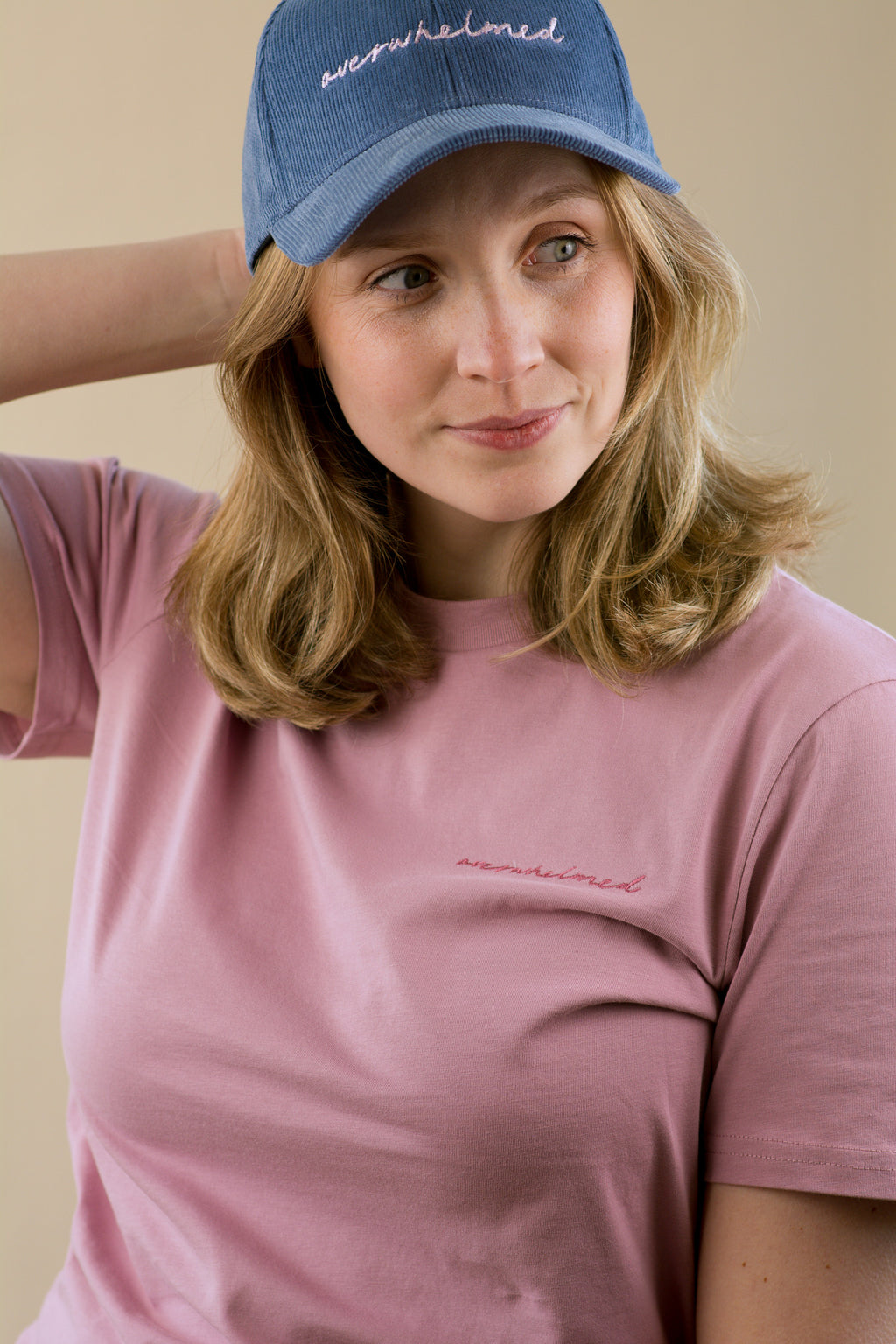 Woman wearing a pink t-shirt and blue cap with text on a beige background