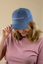 Person wearing a blue cap and pink shirt with 'nowhelmed' branding on a beige background
