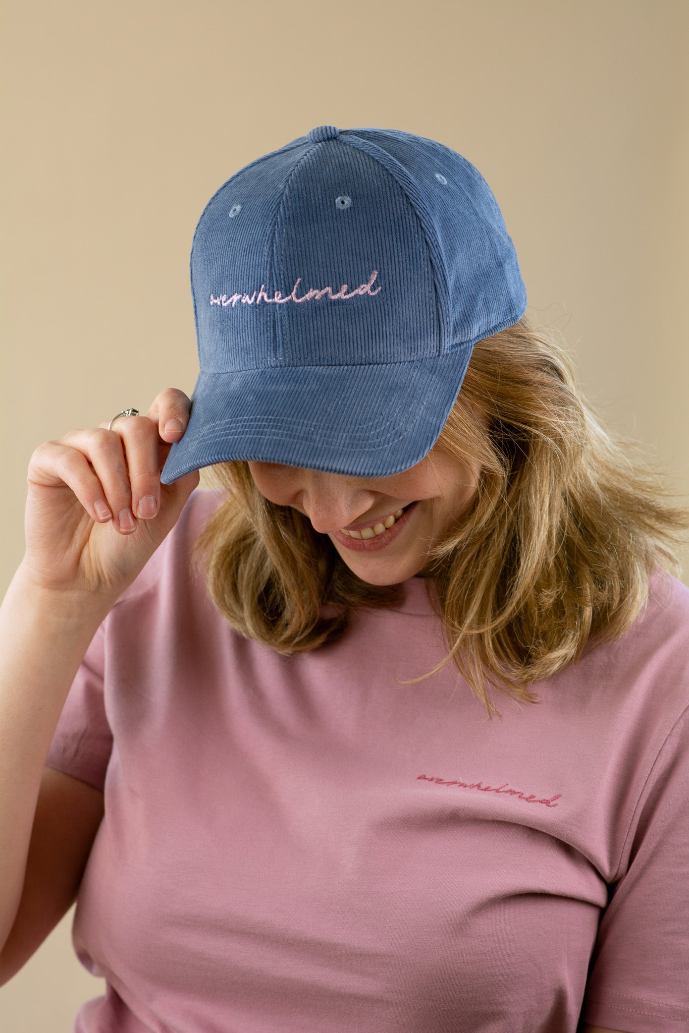 Person wearing a blue cap and pink shirt with 'nowhelmed' branding on a beige background