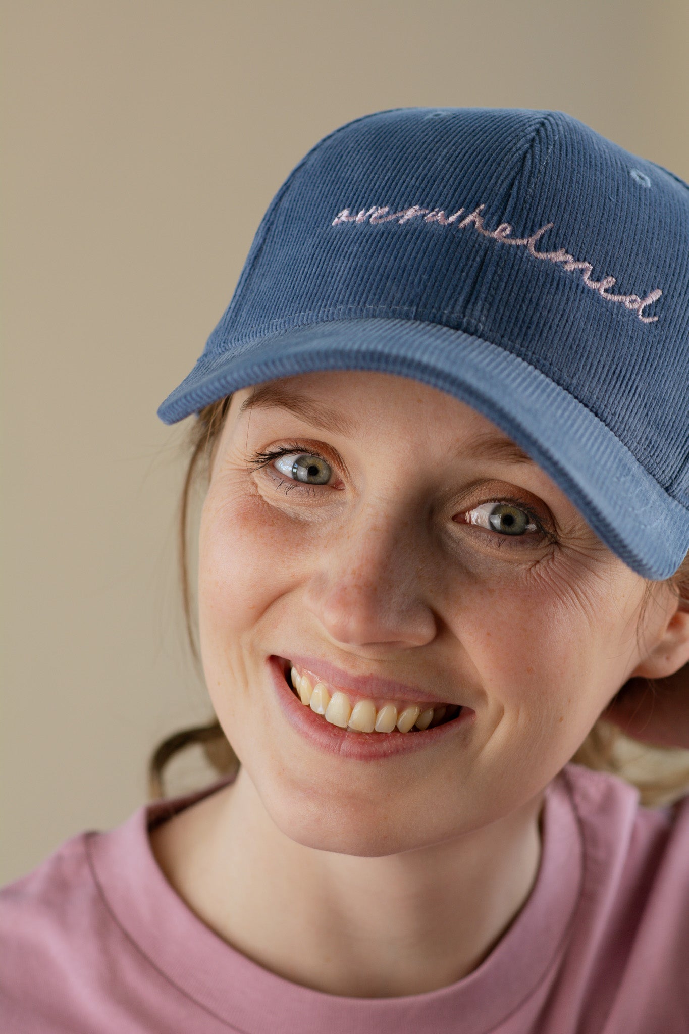 Person wearing a blue cap with embroidered text on a beige background