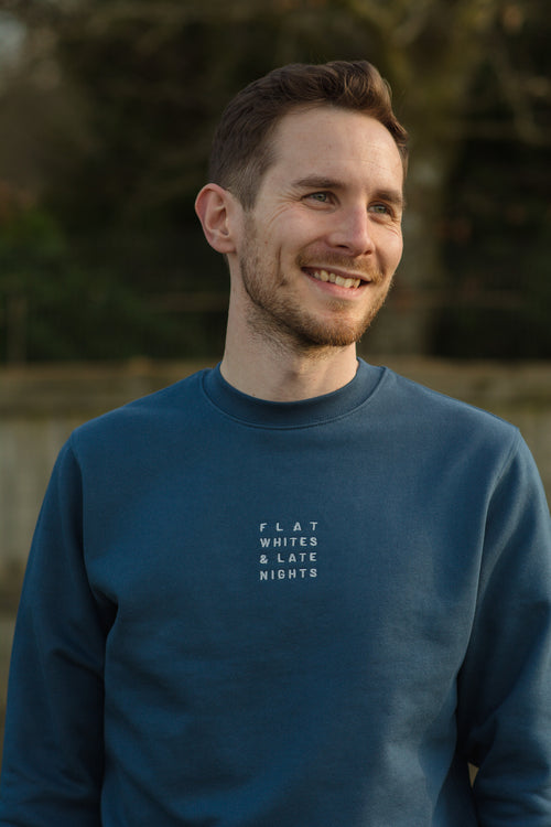 Man wearing a blue sweatshirt with text, standing outdoors with a blurred natural background