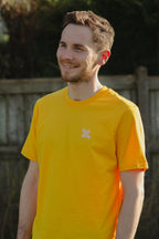 Man wearing a yellow t-shirt with a logo, standing outdoors.
