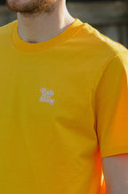 Man wearing a yellow t-shirt with a logo, standing outdoors.