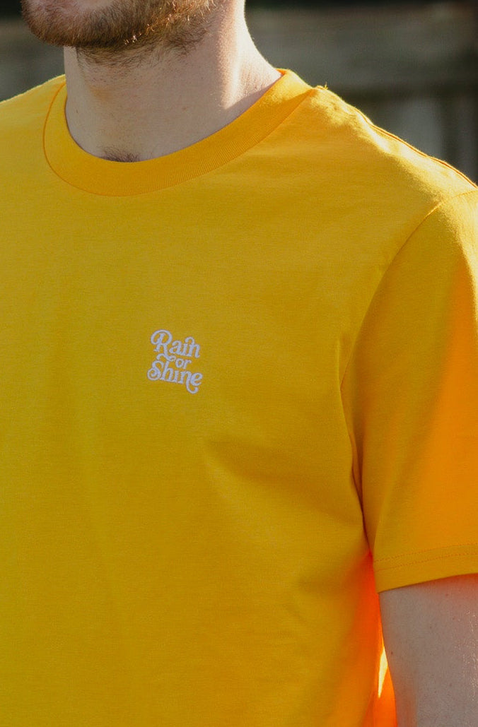 Man wearing a yellow t-shirt with a logo, standing outdoors.